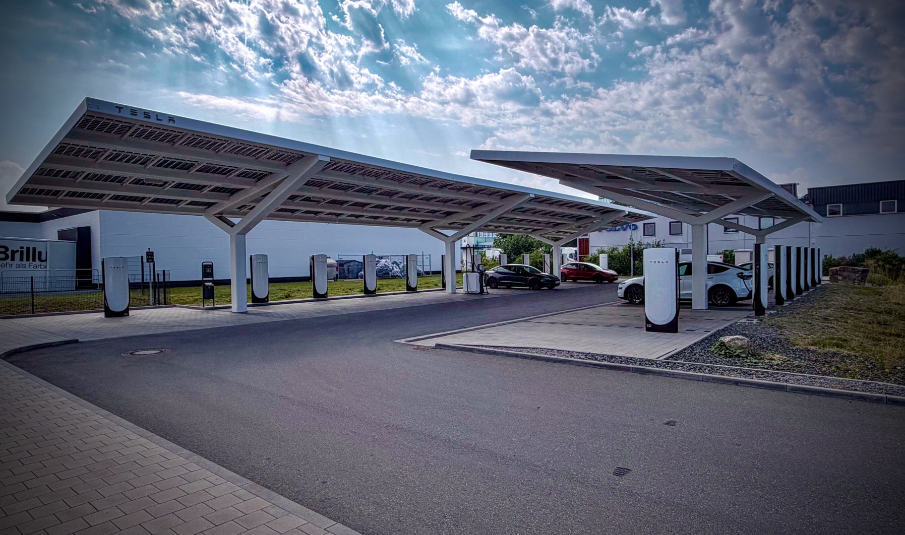 Stacja ładowania Tesla z wiatami fotowoltaicznymi i zaparkowanymi autami przy słupkach ładowarek