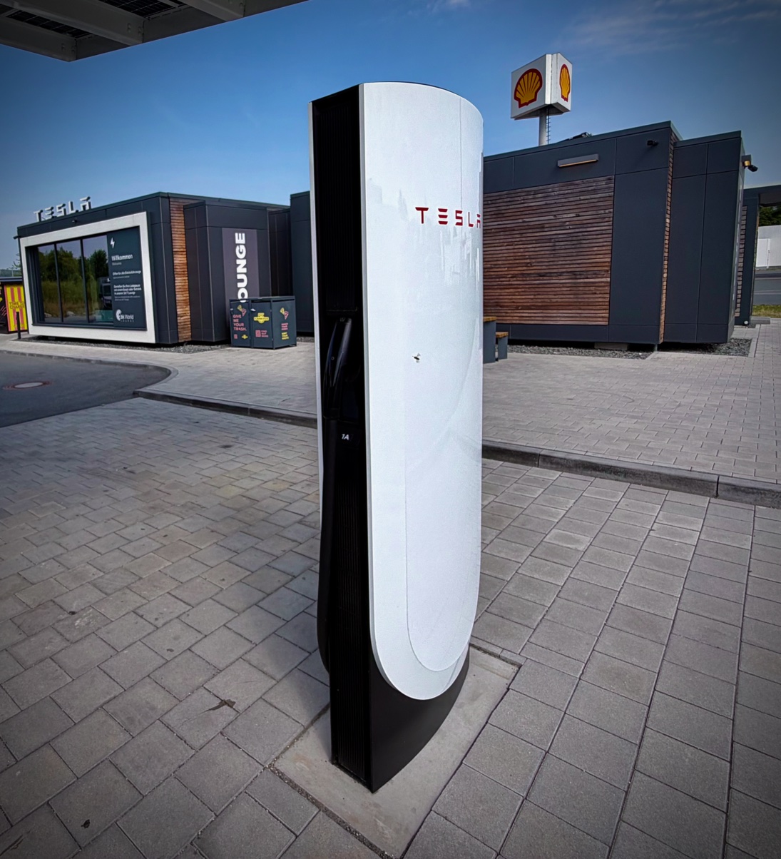 Supercharger Tesla nr 74 sfotografowany pod niskim kątem na wybrukowanej strefie ładowania